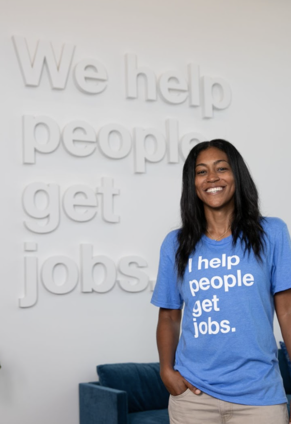 An Indeedian poses in front of a "We help people get jobs" sign